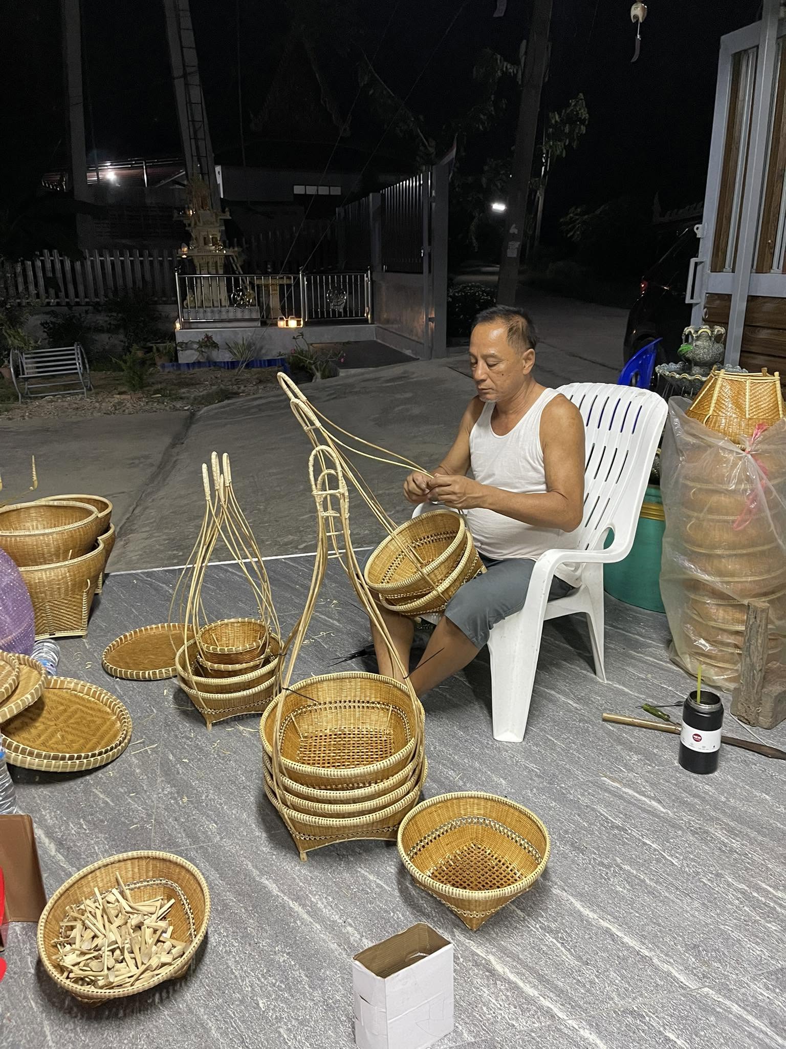 ช่างชายนั่งทำงานจักสานท่ามกลางชิ้นงานหลายรูปทรง